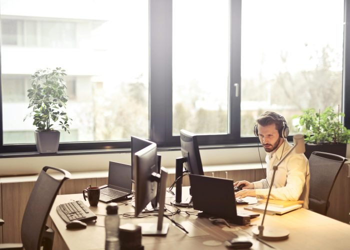 pexels-photo-845451-845451 A businessman sits at a desk using multiple computers and a headset in a well-lit modern office.